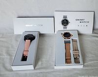 Two smart watches in white packaging boxes showing the watches and extra accessories, with packaging labeled SMART WATCH.