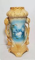 Front and full side view of antique ceramic vase showing hand painted swan scene, rose-shaped handles, and gold gilt accents.