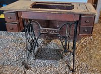 Front view of the Singer sewing cabinet showing the top wood surface with missing sewing machine, six drawers and the cast iron base with 'SINGER' logo.