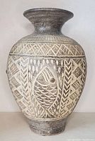 Full view of carved art pottery vase showing the overall shape, gray and beige shades, and carved fish design.
