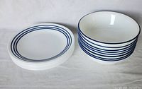 Photo showing 8 bowls and 8 plates with blue band patterns on white Corelle Vitrelle glass