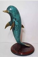 Front and right side view of green patina bronze/brass dolphin figurine on polished wooden tortoiseshell-patterned base