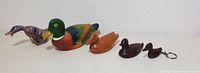 Photo showing five duck figurines in a row, including cloisonné, painted wooden decoy, two dark wooden decoys, and a wooden keychain