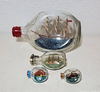 Lot of four vintage pinch glass ship in bottles in various sizes and shapes, showing intricate ship details and wire netting.