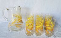 Overall set showing one large glass pitcher and six matching tall glasses, all with yellow and golden wheat print pattern.