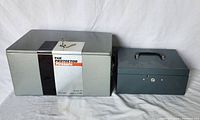 Image shows both the Protector metal fire safe with keys on top and the smaller metal cash box side by side.