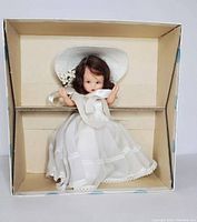 Top-down photo of vintage Nancy Ann Storybook Doll dressed in white lace dress and wide-brimmed hat with floral detail inside original box.