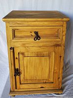 Front view of the rustic wooden end table showing drawer and cabinet door with dark metal rings and natural wood grain.