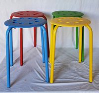 Four stackable stools in red, blue, green, and yellow arranged on white backdrop, showing front and side views of stools.