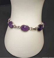Close-up photo of the vintage sterling silver carved cabochon amethyst bracelet displayed on a white bust stand showing details of the amethyst stones and the silver links.