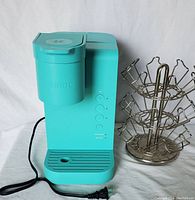 Photo of front and side of the teal Keurig coffee maker and side view of spinning pod storage dispenser