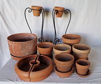 Nine terra cotta pots of varying sizes with some pots paired with matching terra cotta saucers. One large pot, several medium to small pots, and a large divided terra cotta saucer for seed or bulb planting.