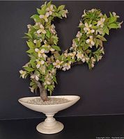 Front view of vintage artificial cherry blossom bonsai tree showing branches, leaves, and flowers in an off-white pedestal planter with white rocks adhered inside.