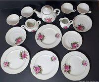 Photo showing all tea set components spread out including plates, saucers, tea cups, sugar bowl, creamer, and teapot with lid on dark background