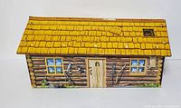 Side view of the vintage Marx Ft Apache tin cabin with yellow shingled roof and detailed log cabin exterior graphics.