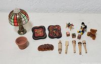Photo showing a variety of miniature dollhouse accessories including stained glass style lamp, trays, bread loaf, flower pot, small toys, and wooden kitchen tools.