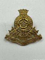 Front and back views of the vintage 17th Duke of York Royal Canadian Hussars brass cap badge, showing details of inscriptions, emblem, crown and attachment loops.