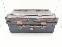 Front view of vintage metal lock-box/travel trunk showing wooden slats, metal construction, and central latch with padlock.