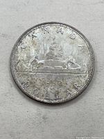 Front side of a 1962 Canadian silver dollar coin showing the voyageur design with canoe and two figures.