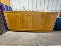 Front view of the solid wood buffet showing four evenly spaced doors with round metal knobs, light wood finish, and base support.