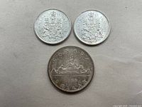Two 1966 Canadian 50 cent coins and one 1966 Canadian silver dollar laid out on flat surface.