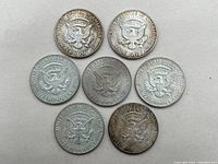 Seven Kennedy Half Dollar coins arranged on a flat surface showing the reverse side with the eagle emblem. Coins show signs of oxidation and wear.