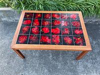 Full view of the vintage Mid-Century Modern teak coffee table with inset red and black tiles on concrete floor near greenery.