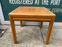 Front angled view of vintage teak side table showing square top and four angled legs in natural warm wood finish.