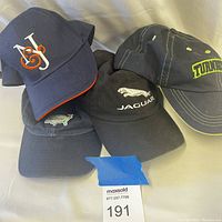 Four sporty hats showing logos and colors including Jaguar, Turner, N & J initials, and a green crocodile on dark caps