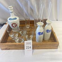 Wooden tray holding six tall narrow beer glasses, four short clear glasses, one porcelain decanter with red cameo design, and two white sake bottles with blue designs.