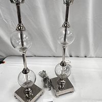 Front view of two glass stacked orb accent lamps on silver metal square bases with attached cords