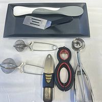 Top-down image showing all kitchen utensils on a dark rectangular plate on a white surface.