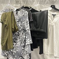 Photo showing various women's clothing hanging on hangers including a green top, a grey patterned dress, black leather pants, and a white blouse.