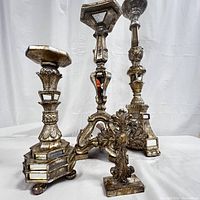 Photo of four gold tone candle stands with mirrored accents and a small ornamental cross, showing intricate baroque-style detailing and varying heights.