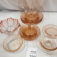 Overall view of the pink glass dinnerware showing plates, bowls and serving pieces with a mix of round and scalloped edges.