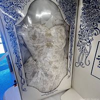 Wedding dress visible in decorative box with blue floral design and plastic window showing beaded bodice