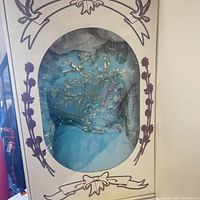 Photo of the full wedding dress in box, shows light blue fabric and silver glitter decoration on bodice and sleeves.