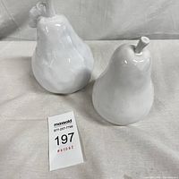 Two white ceramic pears shown side by side on white fabric background, including auction lot tag