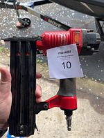 Full side view of the red and black King air nailer held by a person, showing the body, grip, and nail magazine.