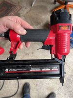 Side view of the red Craftsman Precision Plus 8200B air brad nailer in hand, showing the grip, trigger, and nails magazine with label.