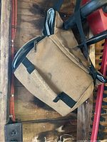Photo showing brown Carhartt lunch box cooler bag hanging from handle, visible dirt on surface and padded strap, black zipper