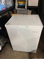 White Insignia chest freezer with closed top lid shown from the front in a garage or storage setting.