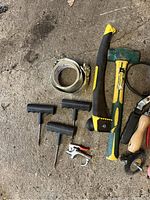 Various hand tools including hammer, T-handle hex keys, staple gun, screwdrivers, wire cutter/stripper, and rolls of tape on concrete floor.