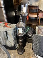 Two tall dark metal candle stands with pointed finials and glass enclosures containing white candles and pinecones.