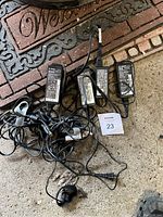 Four IBM Lenovo AC adapter charging cables laid on concrete floor near mat. Cables tangled with one visible wire damage.