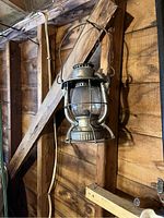 Metal hanging lantern with glass globe and wire frame hanging on wooden wall.