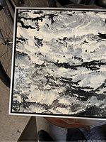 Close-up of textured abstract painting with black, white, and gray impasto strokes, showing detail of the raised paint and framed edges.