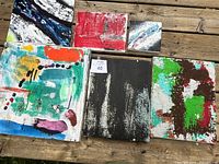 Top view of six abstract paintings laid flat on a wooden surface showing vibrant colors and varied brush techniques