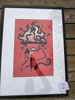 Photo of a framed painting showing a stylized woman wearing a wide-brimmed hat with veil and hearts in a pop art design.