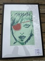Framed modern art print showing a stylized woman with light green hair wearing a red eye patch, in black frame and white mat.